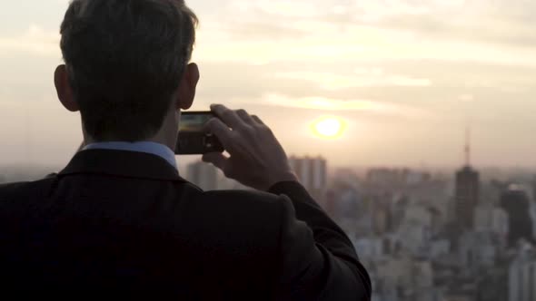 Rear view of businessman taking picture of city with smartphone