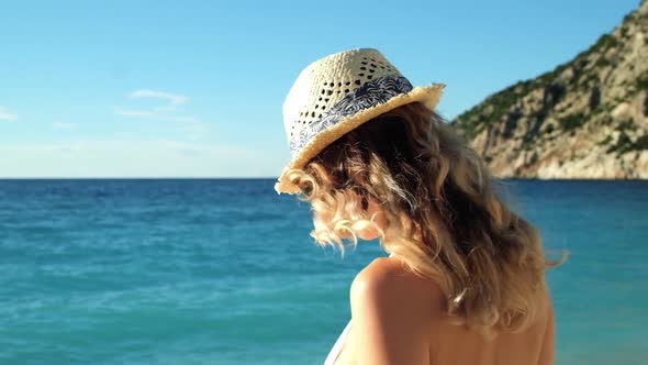 Young beautiful girl in hat and sunglasses standing on beach at sunset