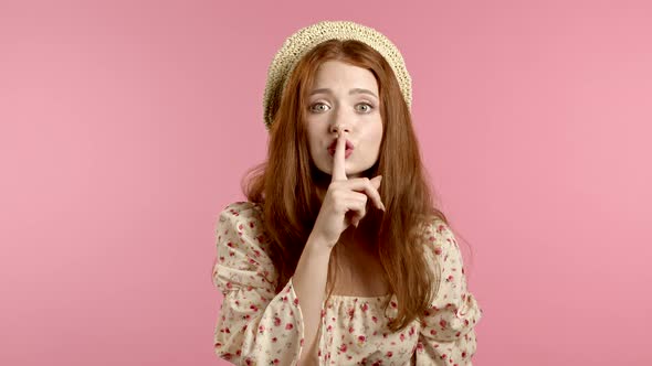 Beautiful Woman in Floral Dress Holding Finger on Her Lips Over Pink Background. Gesture of Shhh