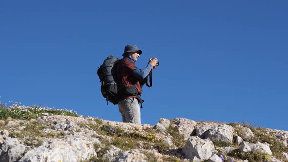 A man in the mountains with a backpack on his back looks at the camera screen