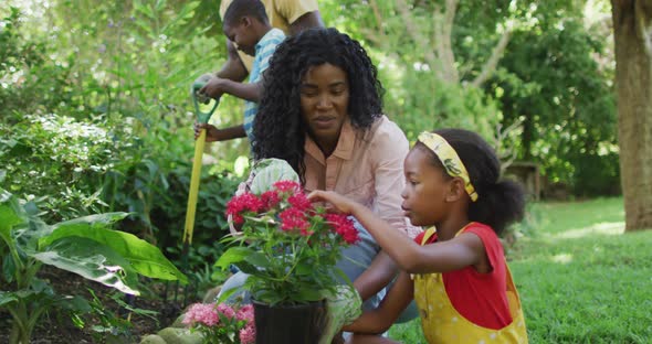 Animation of happy african american mother and daughter planting flowers in garden