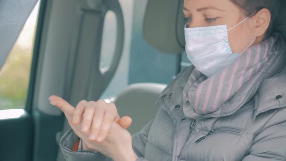 Woman in Car with Surgical Mask on Face Disinfecting Hands