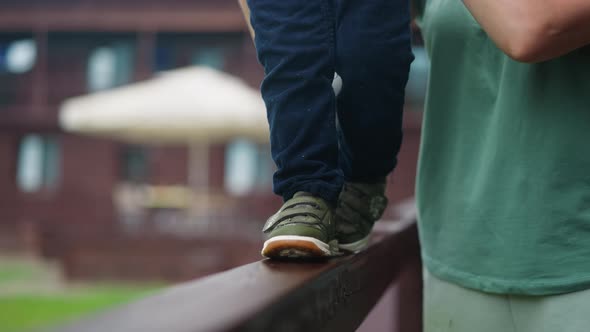 Little Boy Walks Along Wooden Railing with Mother Help