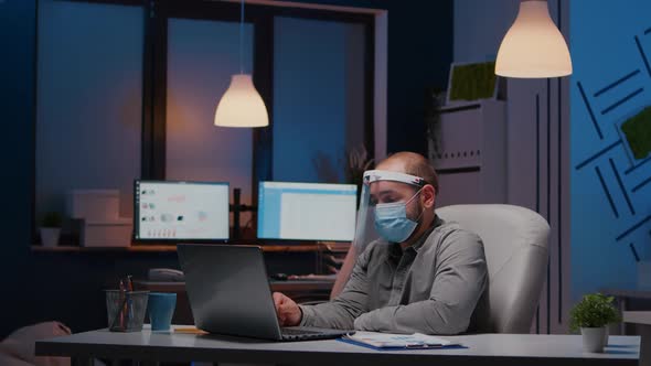 Workaholic Businessman with Face Mask and Visor Against Covid19 Working in Company Office