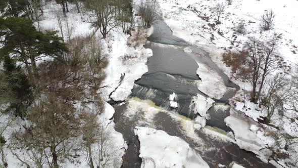 Aerial drone view of a small stream in the winter with snow all around. Recorded in Vahiküla falls i