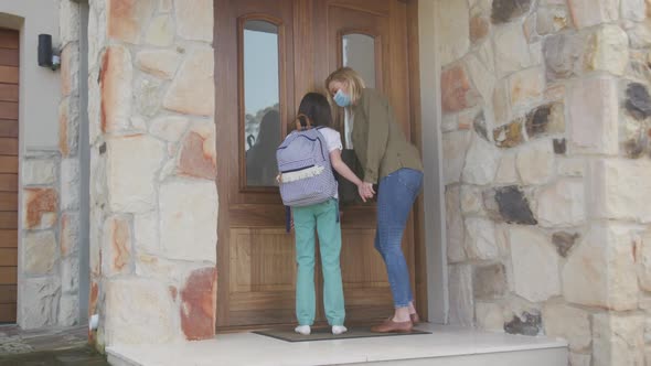 Mother and daughter wearing face masks opening the door of the house