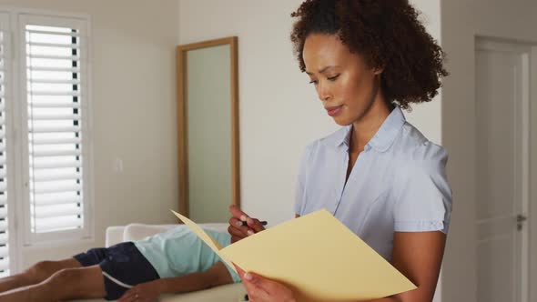 Portrait of mixed race female physiotherapist holding notebook and writing looking at camera