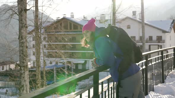 A Woman in a Blue Jacket and a Pink Hat Stands and Smiles on a Winter Street of the City