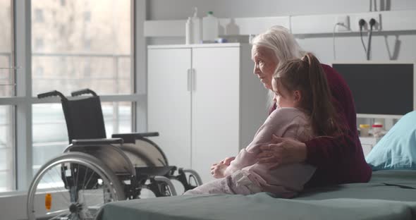 Senior Woman and Little Girl Sitting on Hospital Bed and Hugging