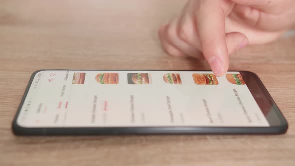 Close Up Of Hand Male Selects Food In Food Online Delivery Apps Directly On Smartphone