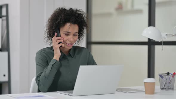 African Woman with Laptop Talking on Smartphone