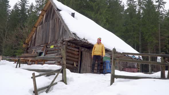 The Traveler Comes Out of a Wooden House in the Winter Forest