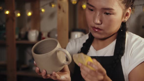 Young Woman Potter Smoothing Out the Clay Cup Using a Wet Sponge