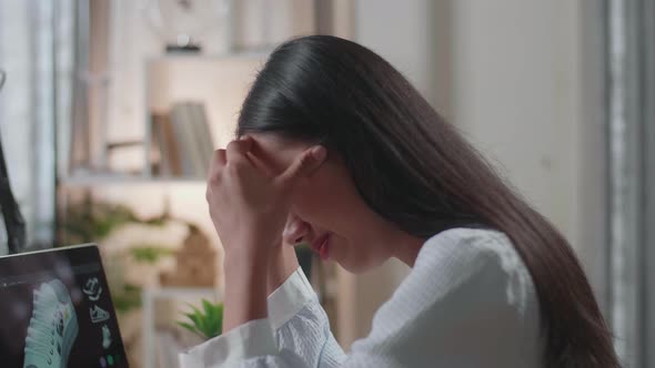 Close Up Of Asian Female Footwear Designer Having A Headache While Designing Shoe On A Laptop