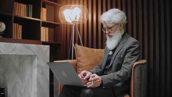 Handsome Elderly Businessman Works at the Laptop Sitting in Modern Place
