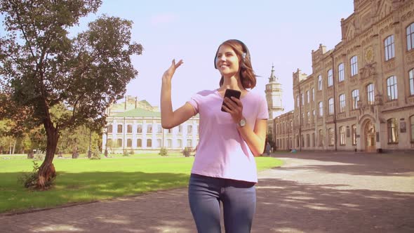 Happy Woman Using Headphones Walks in Campus Area