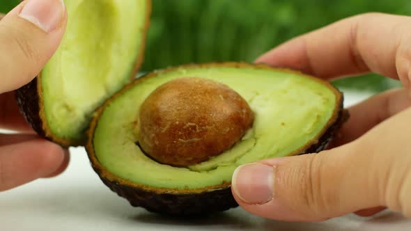 Close-up Women s hands hold two cut halves of fresh Green Avocado Front view