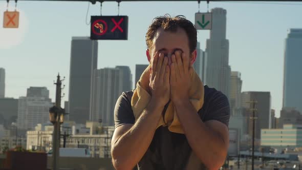 A young man with a beard pouring water over his head after an intense workout.