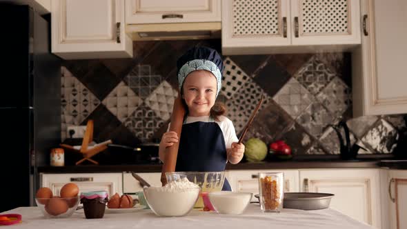 Little Girl with a Rolling Pin in Her Hands Is Preparing Cupcakes in the Kitchen