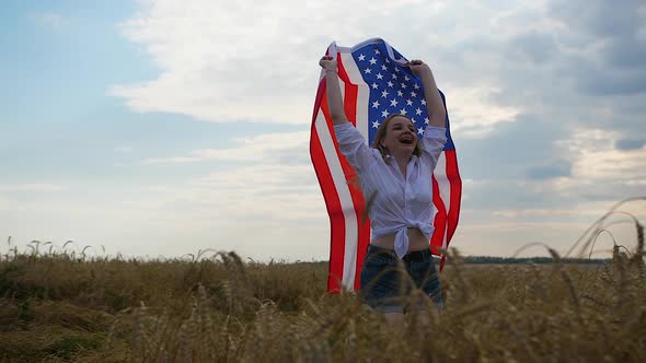 Happy Patriotic Young Woman Waves the US Flag and Jumps Into the Field