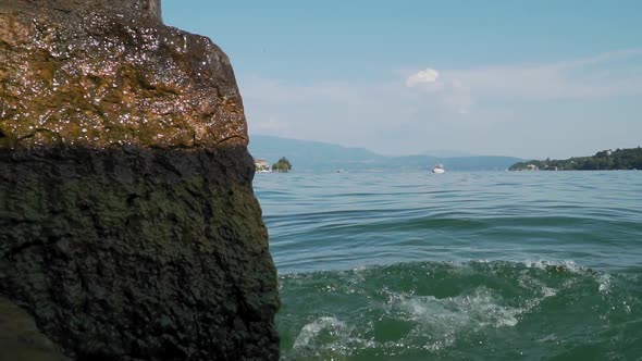 Lake water waves splashing on stone close up, view from shore, lakeside panorama