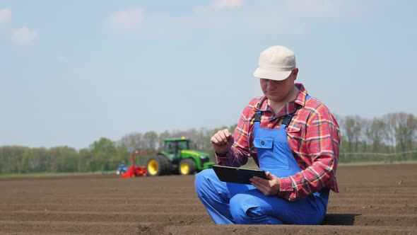 Farmer, Agronomist Sits Between Soil Rows, Checking Quality of Soil on Farm Field. Background of