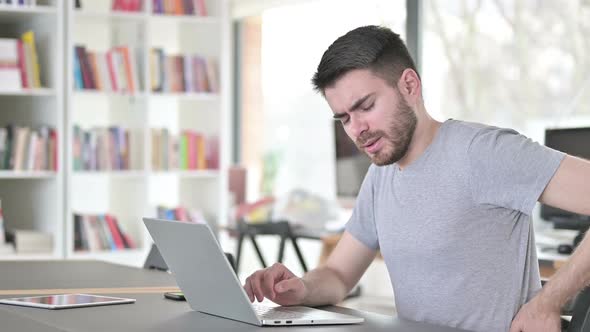 Young Man with Laptop Having Back Pain in Office
