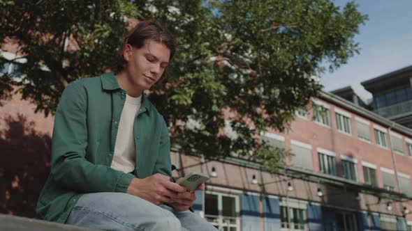 Handsome Man Texting on Smartphone While Sitting Outdoors