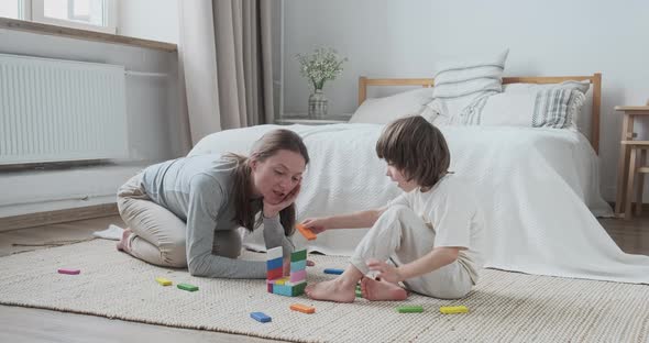 Playful Woman Nanny and Male Kid Constructing Building with Wooden Multicolored Blocks