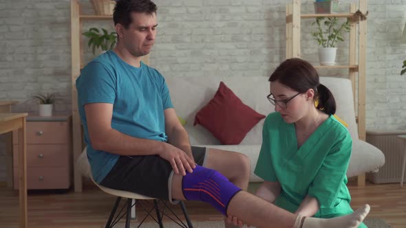 Close Up of the Nurse Helps To Pull the Bandage on the Knee of a Man Athlete