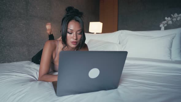 Woman Freelancer with Computer Lying on a Bed in Hotel Room