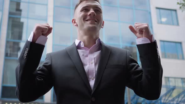 Portrait of Excited Smiling Businessman Gesturing Victory Standing at Business Center Outdoors