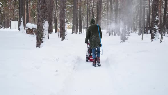 Man Cleans Park Road Walking with Snow Blower and Shovel