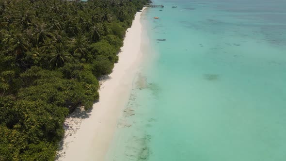 Drone flight over the coast of the Maldivian island, blue water against a beautiful sky and a pier i