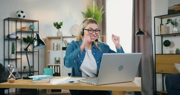 Young Woman in Headset and Glasses Seeing Good News on Laptop Screen