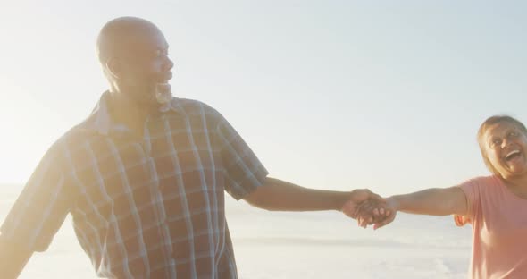 Smiling senior african american couple holding hands and walking on sunny beach