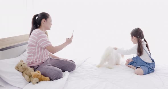 Mother and daughter playing with white dog on bed 3
