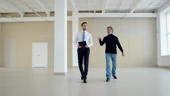 Businessman and manager walk around an empty warehouse discussing business, front view.