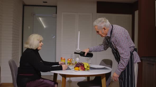 Senior Retired Couple Having Fun Drinking Wine and Eating Meal During Romantic Supper in Kitchen