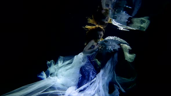 a Slowmotion Underwater Shot of a Young Woman Swimming in a Pool in a Chiffon Dress