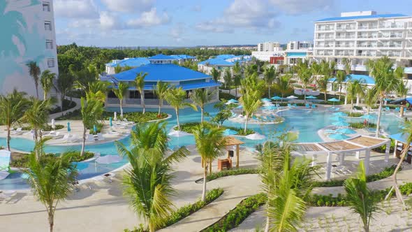 Aerial panning shot showing empty swimming pools with palm trees during sunny day - Covid-19 Pandemi