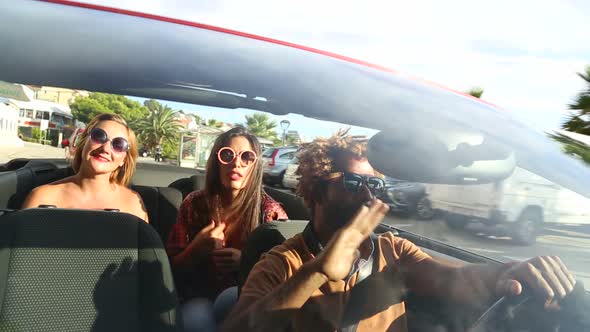 Young people singing and dancing in red convertible looking for parking space