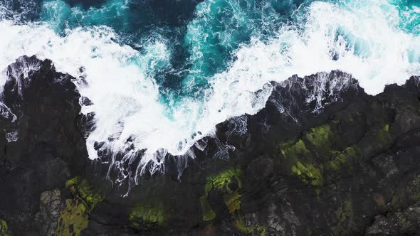 Aerial View of Waves Break on Rocks of Faroe Islands Cliffs in a Blue Ocean