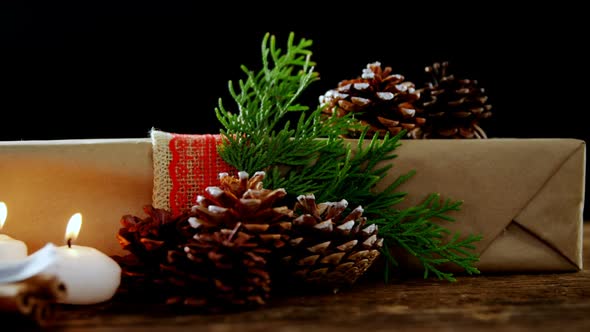 Burning candles, gift box and pine cones against black background