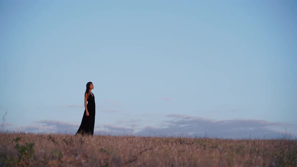 Side View of a Beautiful Brunette Model in Long Black Dress Going Towards the Sun