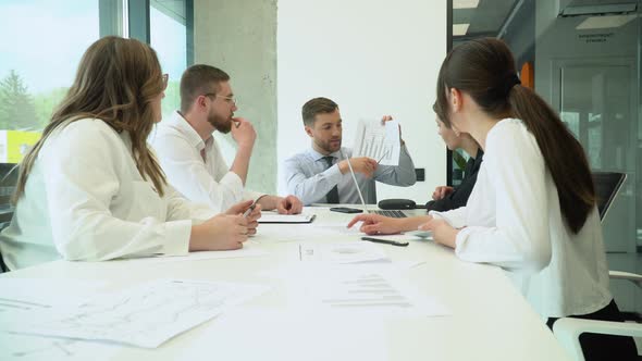 A Group of Young Male and Female Office Employees Sitting and Discussing on a Project in a