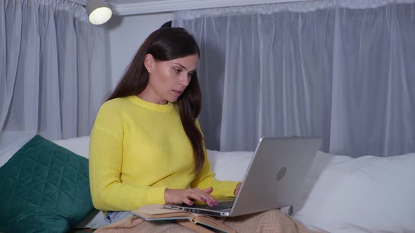Woman Is Learning Online with the Teacher Using Video Call on Laptop While Sitting on Bed with