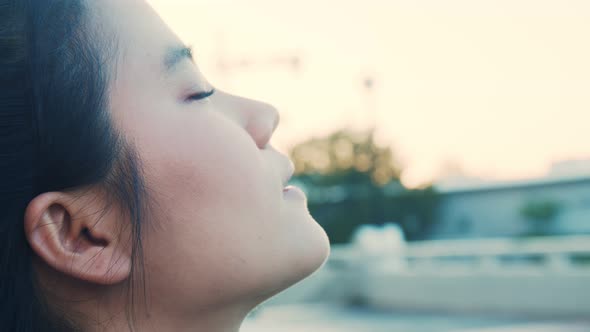 Attractive Asian sportswoman keeping eyes closed and breathing fresh air at the park.