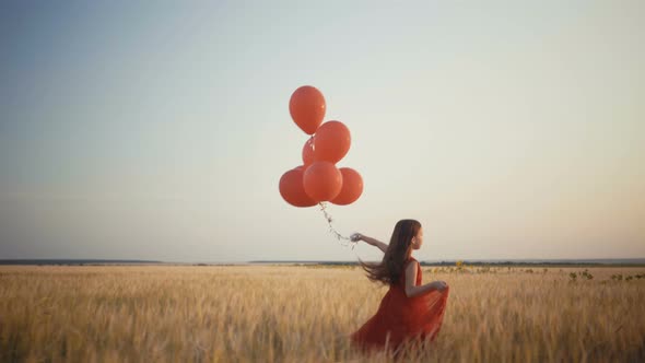 Happy Young Girl with Balloons Running in the Wheat Field at Sunset.  Video.