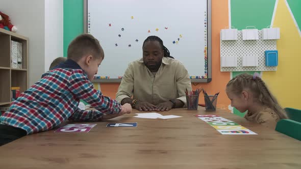 African American Teacher and a Group of Children are Learning Numbers While Sitting at the Table in